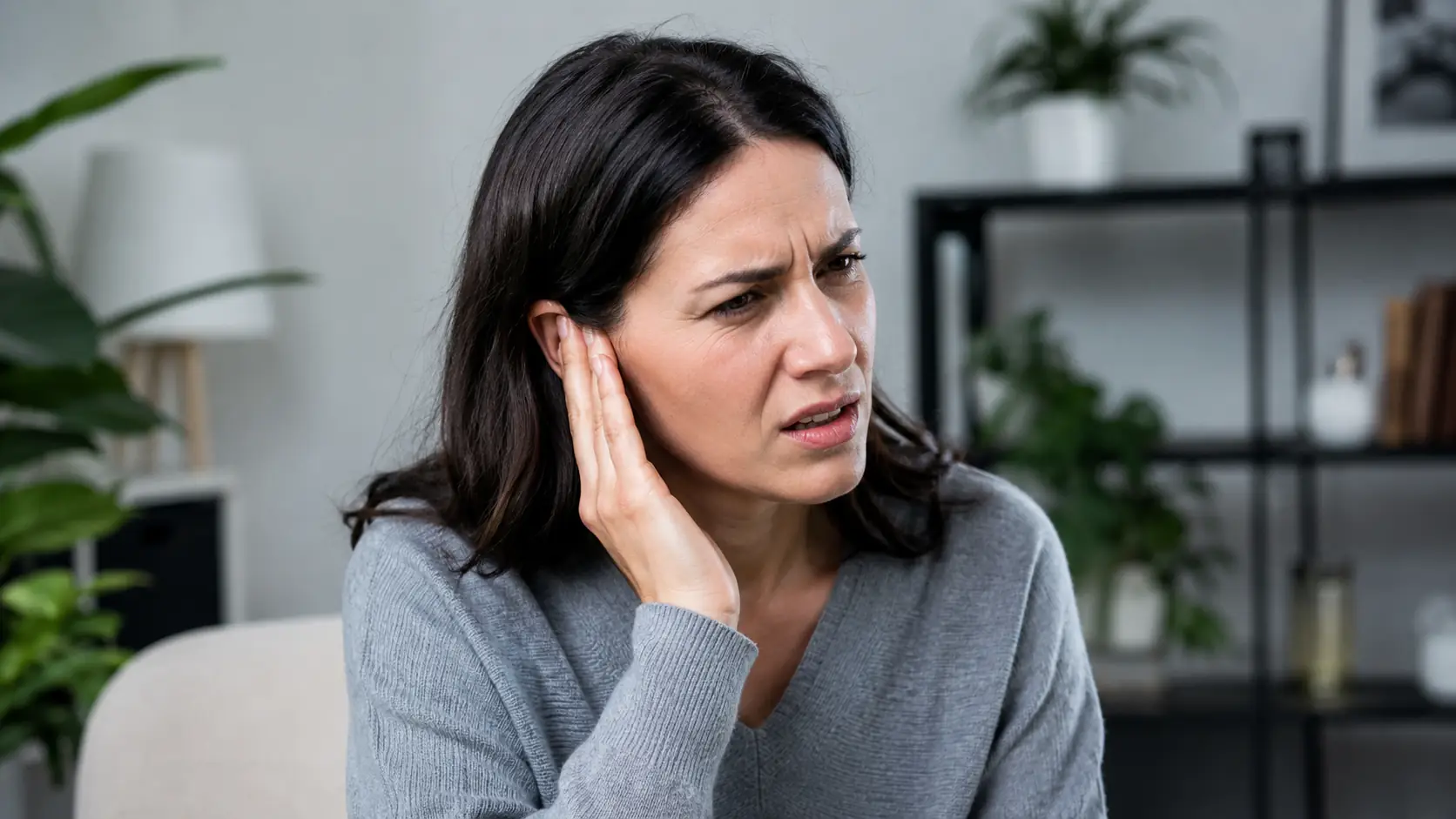 Person hält sich wegen eines plötzlichen Pfeifens die Hand ans Ohr als mögliches Anzeichen für Tinnitus Symptome